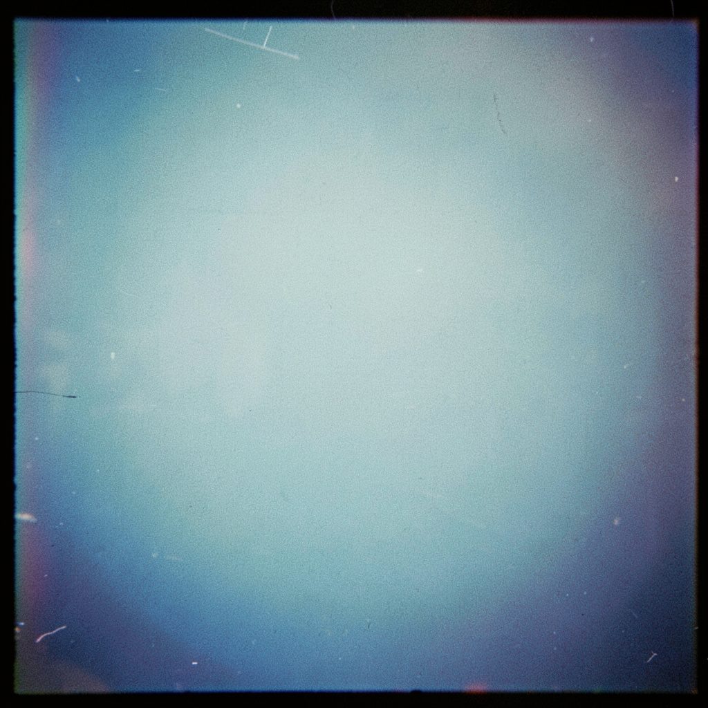 A grainy color photograph of a baseball sitting in the dirt near home plate, the catcher's shadow falling across the batter's box.