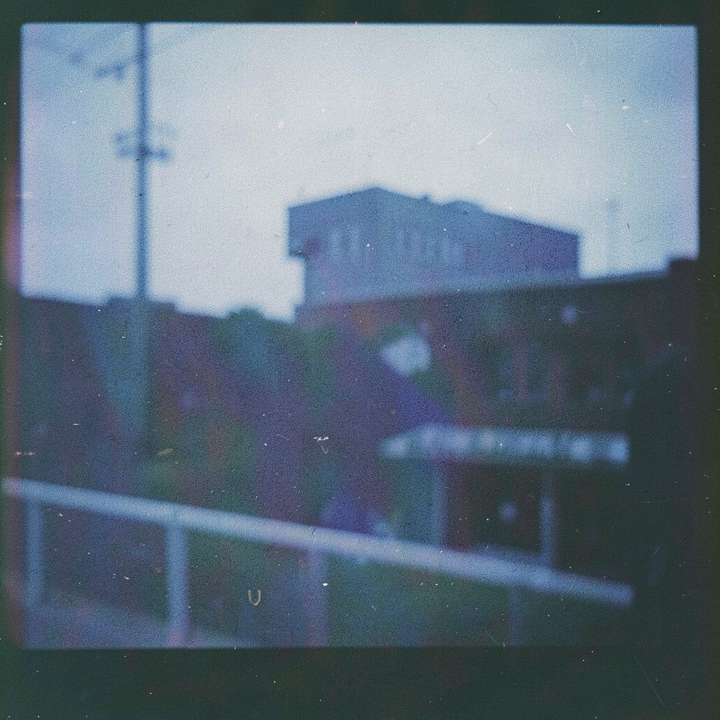 A grainy film photograph of a left-handed pitcher winding up, the stadium lights glowing against a twilight sky.